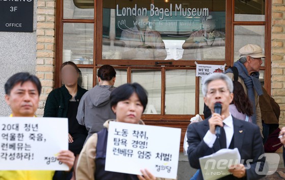 30일 서울 종로구 런던베이글뮤지엄 매장 앞에서 권영국 정의당 대표가 런던베이글뮤지엄 청년 노동자 과로사 규탄 및 책임 촉구 기자회견을 하고 있는 가운데, 런던베이글뮤지엄 매장 안에서 청년 노동자들이 업무를 하고 있다.
